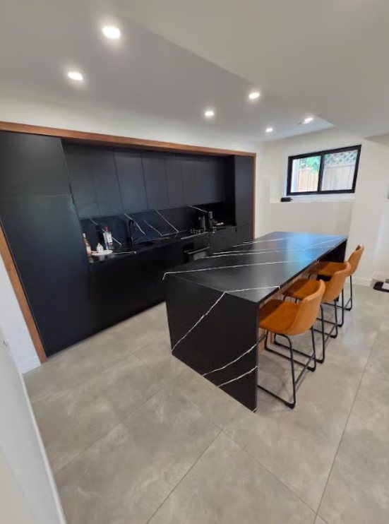 Matte black kitchen cabinetry with warm wood surround and stone island